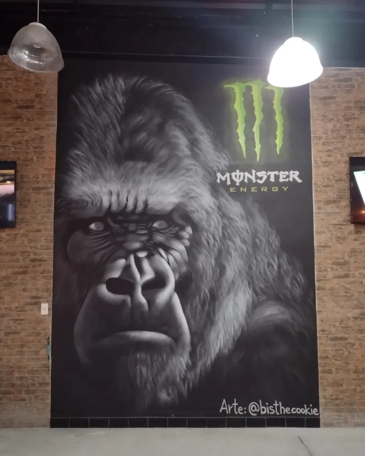 Gorila realista pintado em preto e branco numa parede escura, com o logo da Monster Energy acima