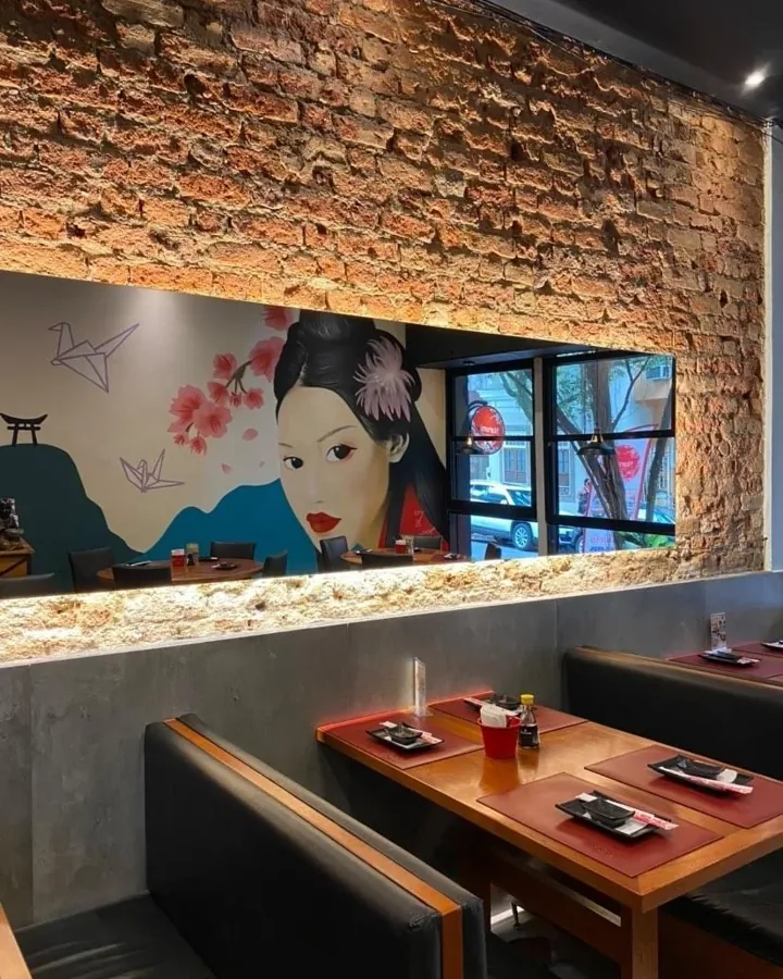 Salão do restaurante japonês com parede de tijolo e o mural da gueixa ao fundo