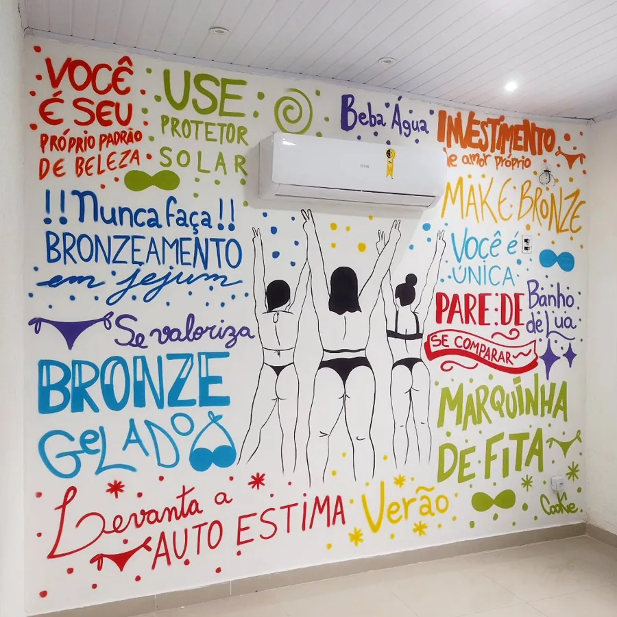 Parede de estúdio de bronzeamento com frases coloridas e silhuetas de três mulheres de biquíni