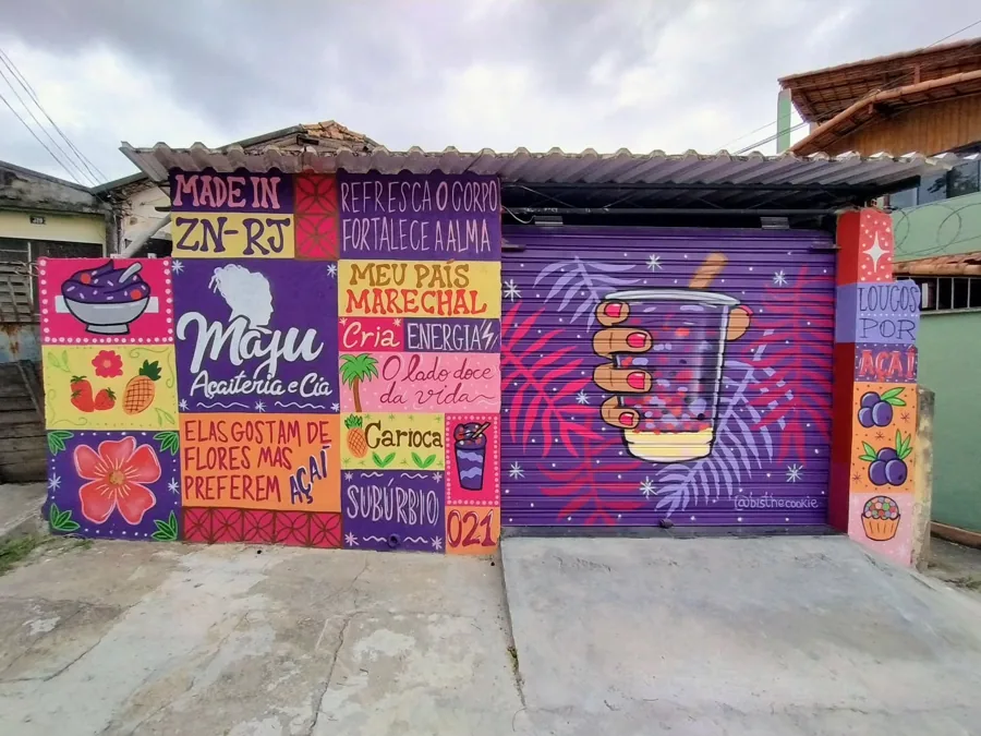 Fachada de açaiteria toda pintada com lettering colorido, frutas e um copo de açaí na porta de aço roxa