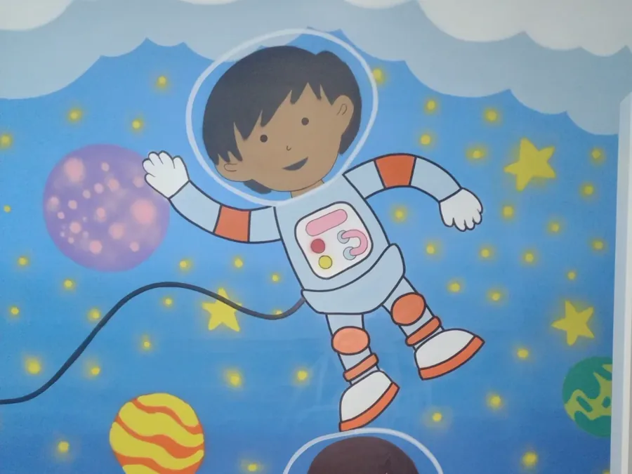 Detalhe: menino astronauta acenando, cercado de estrelas e planetas