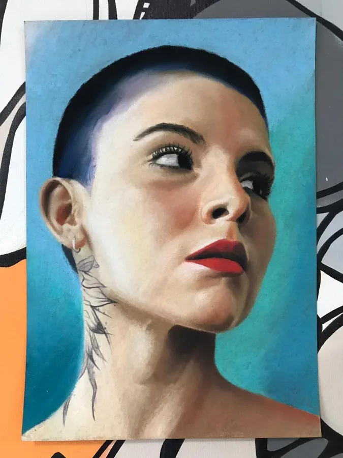 Retrato realista em pastel de uma mulher de cabelo raspado e batom vermelho, olhando para o lado, sobre fundo azul